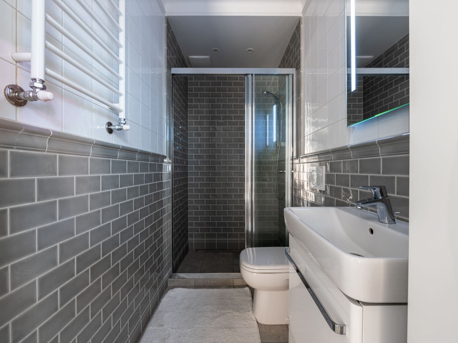 Narrow bathroom lined floor to ceiling in grey brick-bond wall tiles with a walk-in shower