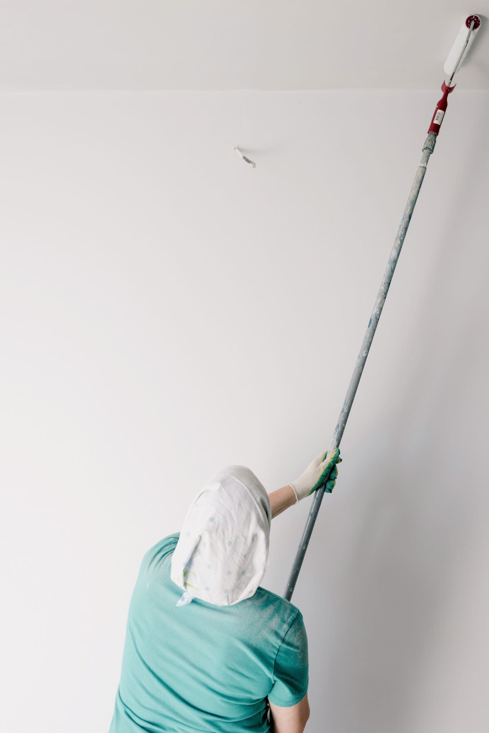 Painter using an extension roller to lay a fresh coat across a high ceiling